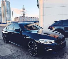 a black bmw car parked in front of a building with other cars behind it on the street