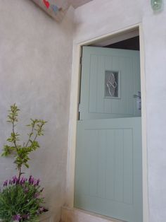 a green door is open on the side of a white building with potted plants