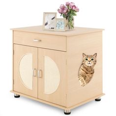 a cat sitting on top of a wooden cabinet next to a vase with pink flowers