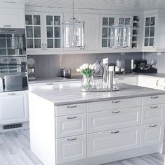 a kitchen with white cabinets and countertops has flowers in vases on the island