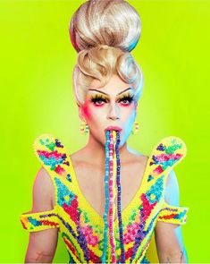 a woman with bright makeup and colorful hair is holding a pipe in front of her mouth