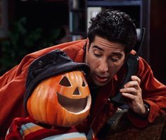 a man talking on a cell phone next to a carved pumpkin