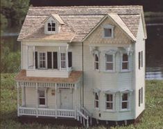 a white doll house sitting on top of a lush green field next to a lake