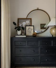 a dresser with a mirror, lamp and pictures on it