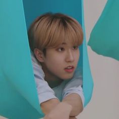 a young man with blonde hair is looking out from behind a blue curtain