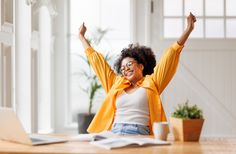 a woman sitting at a desk with her arms in the air