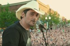 a man wearing a cowboy hat and holding a microphone in front of a large crowd