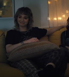 two women sitting on a couch in front of a window, one holding a pillow