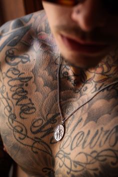 a man with tattoos on his chest wearing a silver necklace and sunglasses is looking at the camera