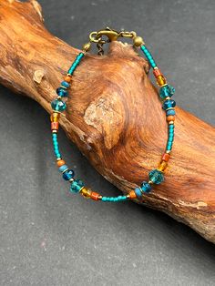 a bracelet with turquoise and orange beads on a wooden branch next to a piece of wood