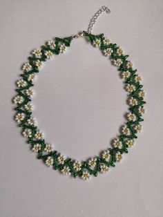 a green and white beaded necklace on a silver chain with small yellow and white flowers