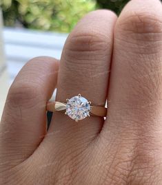 a person's hand with a diamond ring on their finger, showing the center stone