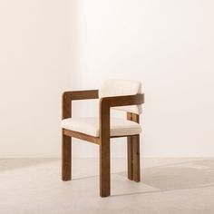 a wooden chair with a white upholstered seat and back rest in front of a wall