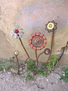 three metal flowers sitting next to each other on top of a cement wall with green plants growing out of it