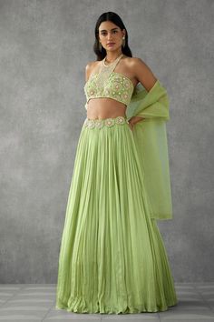 Green sleeveless jewelled halter neck padded blouse in tulle base with floral applique work using sequins, pearls and beads. Paired with floral applique waistband pleated flare cancan lehenga in georgette crepe base and dupatta.
Components: 3
Pattern: Applique, Embroidery
Type Of Work: Floral, Pearls
Neckline: Halter Neck
Sleeve Type: Sleeveless
Fabric: Lehenga: Georgette Crepe, Blouse and Dupatta: Organza
Color: Green
Other Details: 
Attached inner lining
Padded blouse
Attached cancan
Approx. w Pithi Outfit Brides, Pleated Blouse Designs, Green Floral Lehenga, Slumdog Millionaire, Cancan Lehenga, Floral Lehenga, Halter Blouse, Lehenga Designs Simple, Applique Work