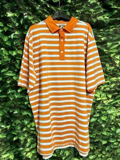 an orange and white striped polo shirt hanging on a green wall with ivy growing behind it