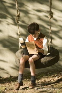 a young boy sitting on a swing reading a book