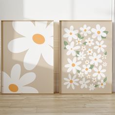 two framed pictures with daisies on them in front of a white wall and wooden floor