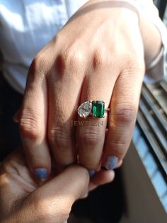 a woman's hand holding an emerald and diamond ring