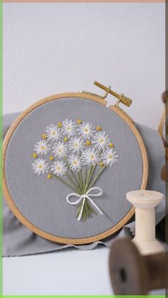 a close up of a flower on a pillow near a thread spool and sewing needle