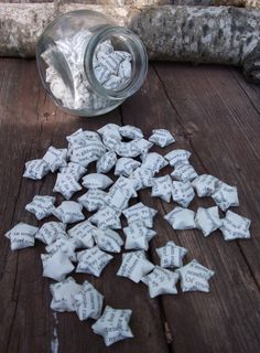 a glass jar filled with lots of white paper hearts on top of a wooden table