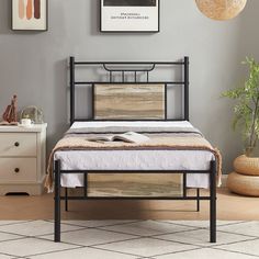 a black metal bed frame with wooden slats in a gray bedroom, next to a white dresser and potted plant