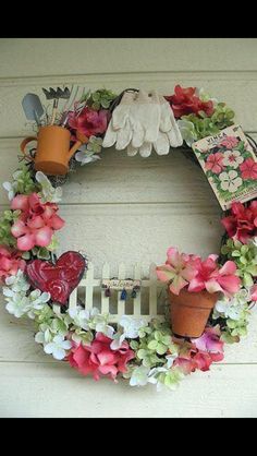 a wreath is hanging on the side of a house with flowers and gardening utensils