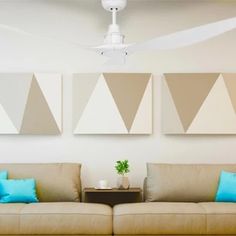 a living room with two couches and a ceiling fan in front of three paintings on the wall