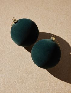 two dark green balls sitting on top of a tan surface with a gold ring around them