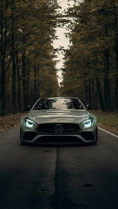 the front end of a mercedes sports car on a road with trees in the background