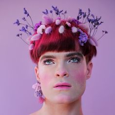 a woman with red hair and purple flowers in her hair, wearing pink earrings on her head