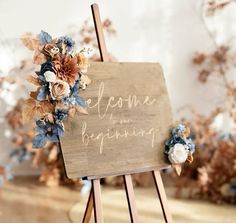 a welcome sign with flowers on it in front of a wooden easel that says welcome to the beginning