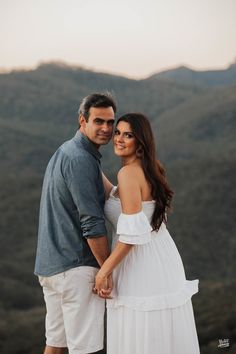 a man and woman standing next to each other on top of a mountain holding hands