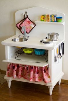 a toy kitchen with sink, stove and dishes on the shelf in front of it