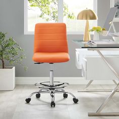 an orange office chair sits in front of a desk with a lamp and potted plant