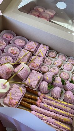 a box filled with lots of pink and gold decorated cookies next to cupcakes