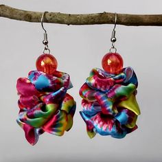 pair of earrings with colorful fabric and glass bead hanging from hooks on tree branch