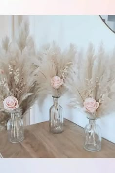 three glass vases with flowers in them sitting on a wooden table next to a mirror