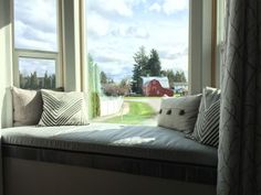 a window seat with pillows on it in front of two windows and a barn view