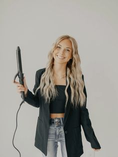 a woman holding a hair dryer in her hand and smiling at the camera while standing against a white wall