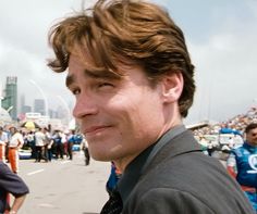 a man standing in front of a crowd wearing a black shirt and tie with his head tilted to the side