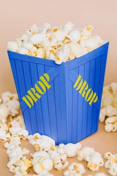 a blue box filled with popcorn sitting on top of a table next to a pile of popcorn