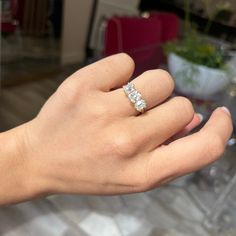 a woman's hand with a diamond ring on top of her finger and a plant in the background