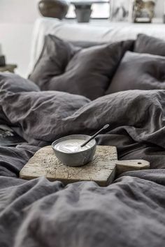 a bowl of yogurt sits on a wooden board in the middle of a bed