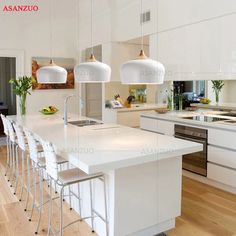 a large kitchen with white cabinets and counter tops, along with bar stools that match the hardwood flooring