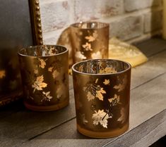 two gold colored cups sitting on top of a wooden table next to a framed mirror