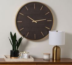 a large clock on the wall above a table with a lamp and potted plant