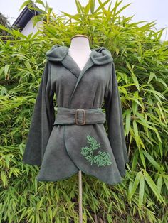 a green robe is sitting on top of a wooden stand in front of some plants