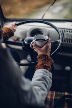 a person driving a car with a cup in their hand