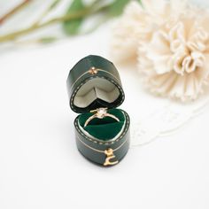 an open ring box sitting on top of a white table next to a flower bouquet